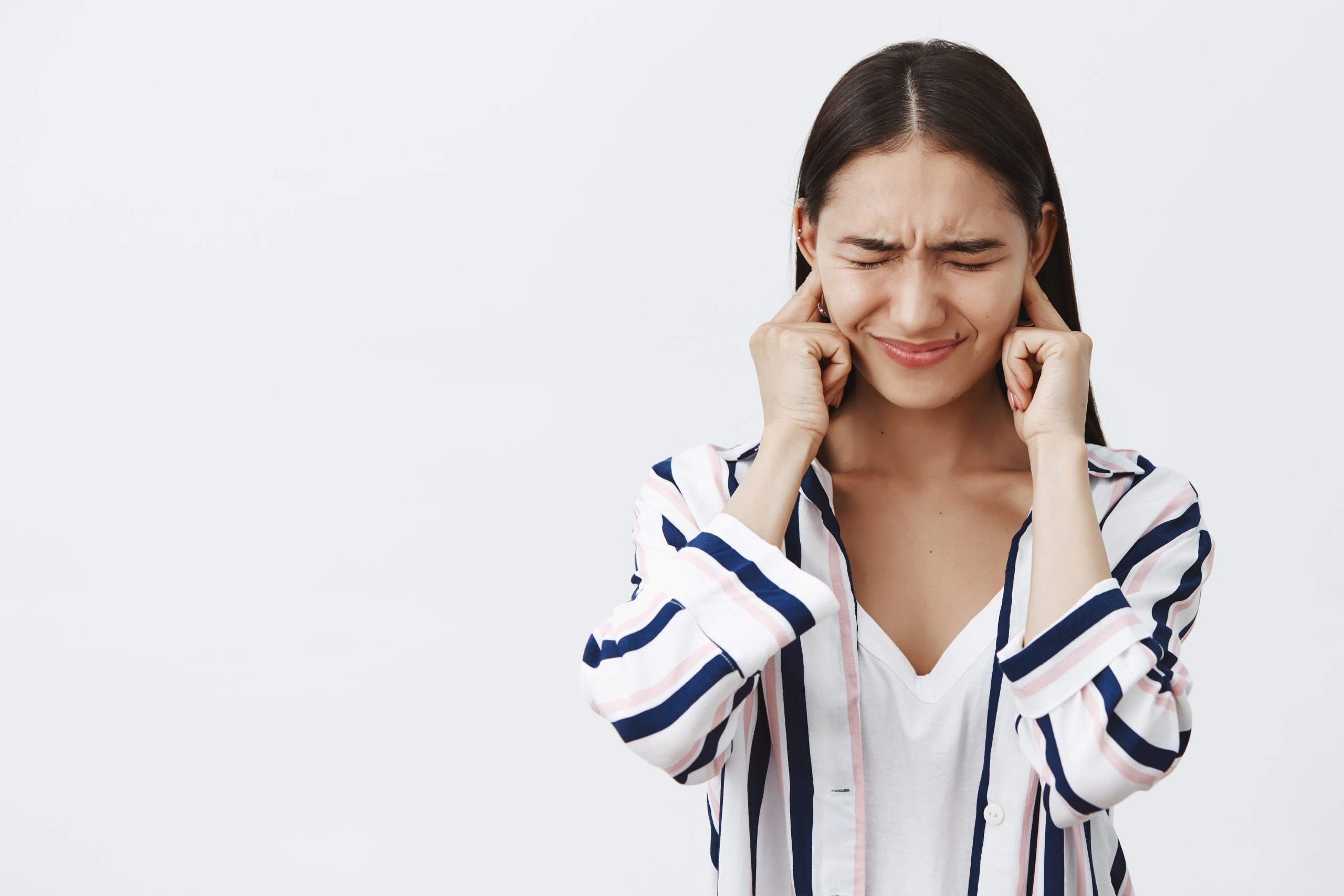 Daughter covering ears being displeased of loud fight of parents, feeling intense and timid. Portrait of unhappy and sad cute woman in blouse, frowning with closed eyes trying not hear noise